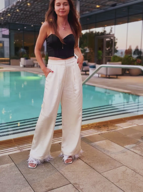 Model walking and sitting in handcrafted ivory satin wide-leg pants, highlighting the fluid movement and elegant drape of the fabric.